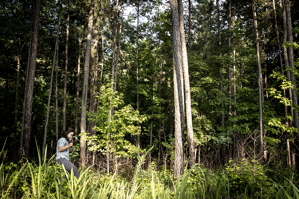 Young woman carrying LiDAR equipment in a research forest