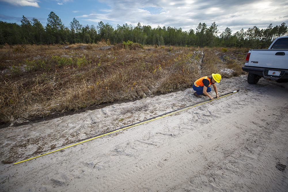 Terri Hall measures a pole laid on dirt road