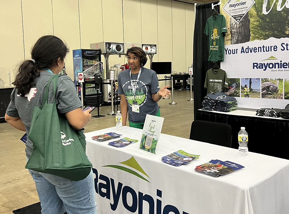 Ebony behind New England Forestry table speaking to student