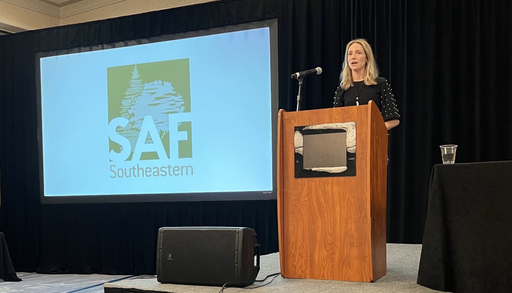 Shawn stands at a podium. A screen in the background displays the SAF logo.