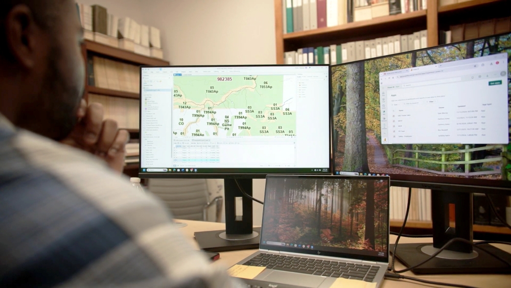 Employee Aaron views two screens with data from sensing and mapping the forest.