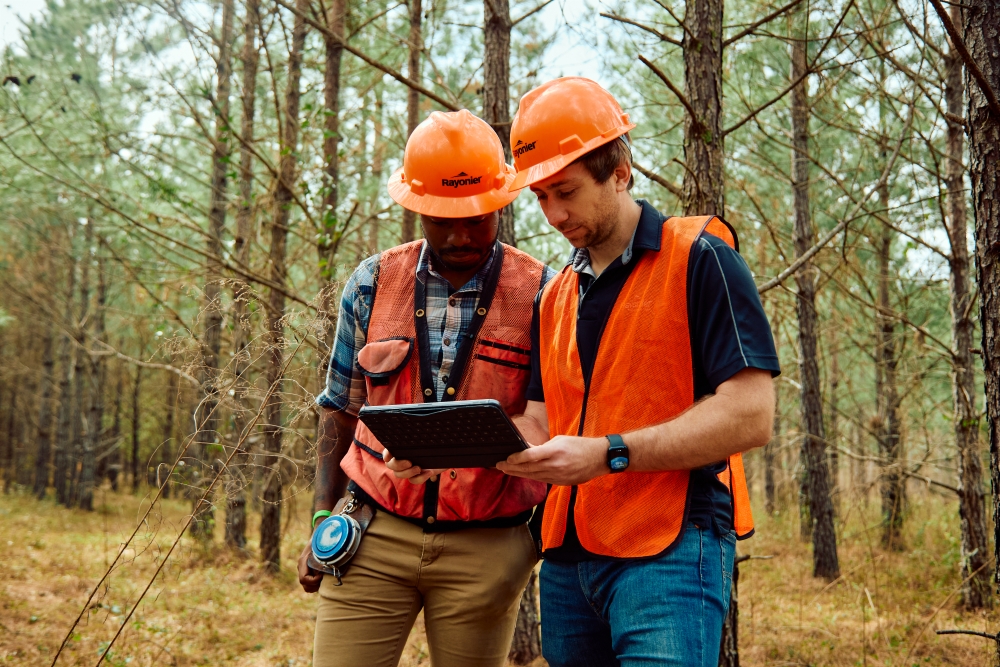 Aaron and Trevor stand in a forest reviewing data on a tablet.